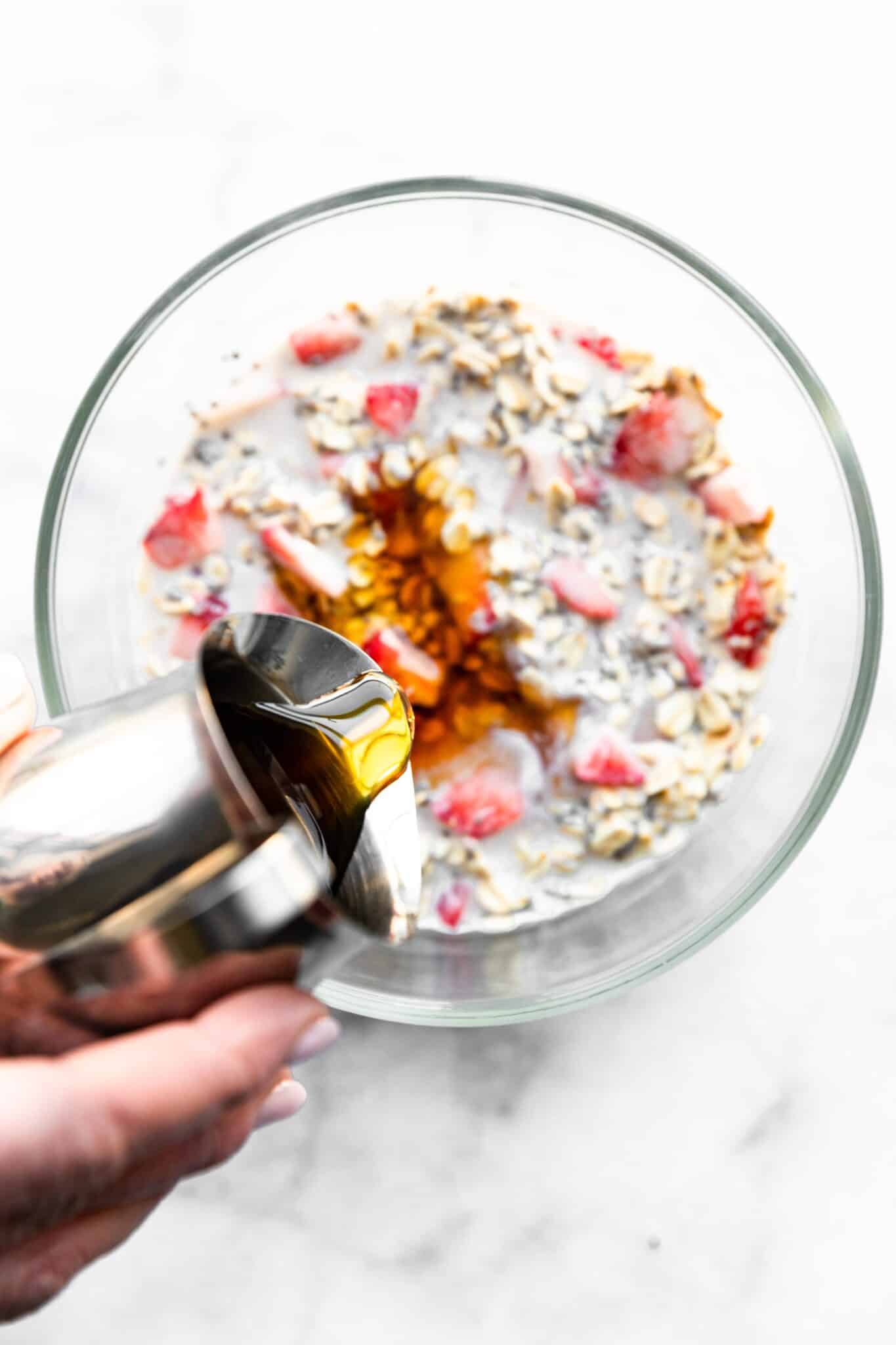 Overhead photo of maple syrup being poured into strawberry overnight oats.