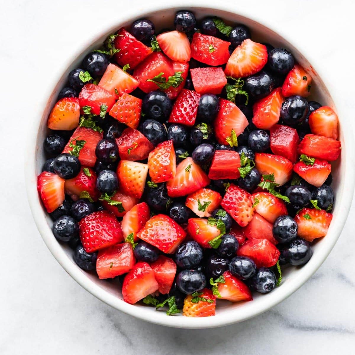 A photo of a bowl of summer berry salad sitting on a marble counter.