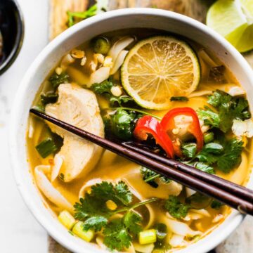 Overhead photo of chopsticks in a white bowl of Thai Chicken Soup on wooden board.