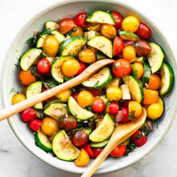 a salad with tomatoes and zucchini with wooden spoons tucked in