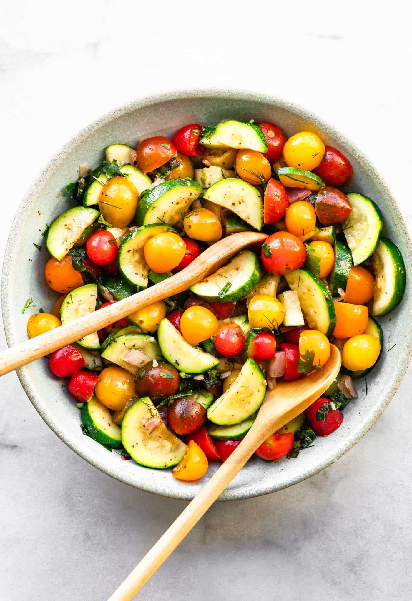 a salad with tomatoes and zucchini with wooden spoons tucked in