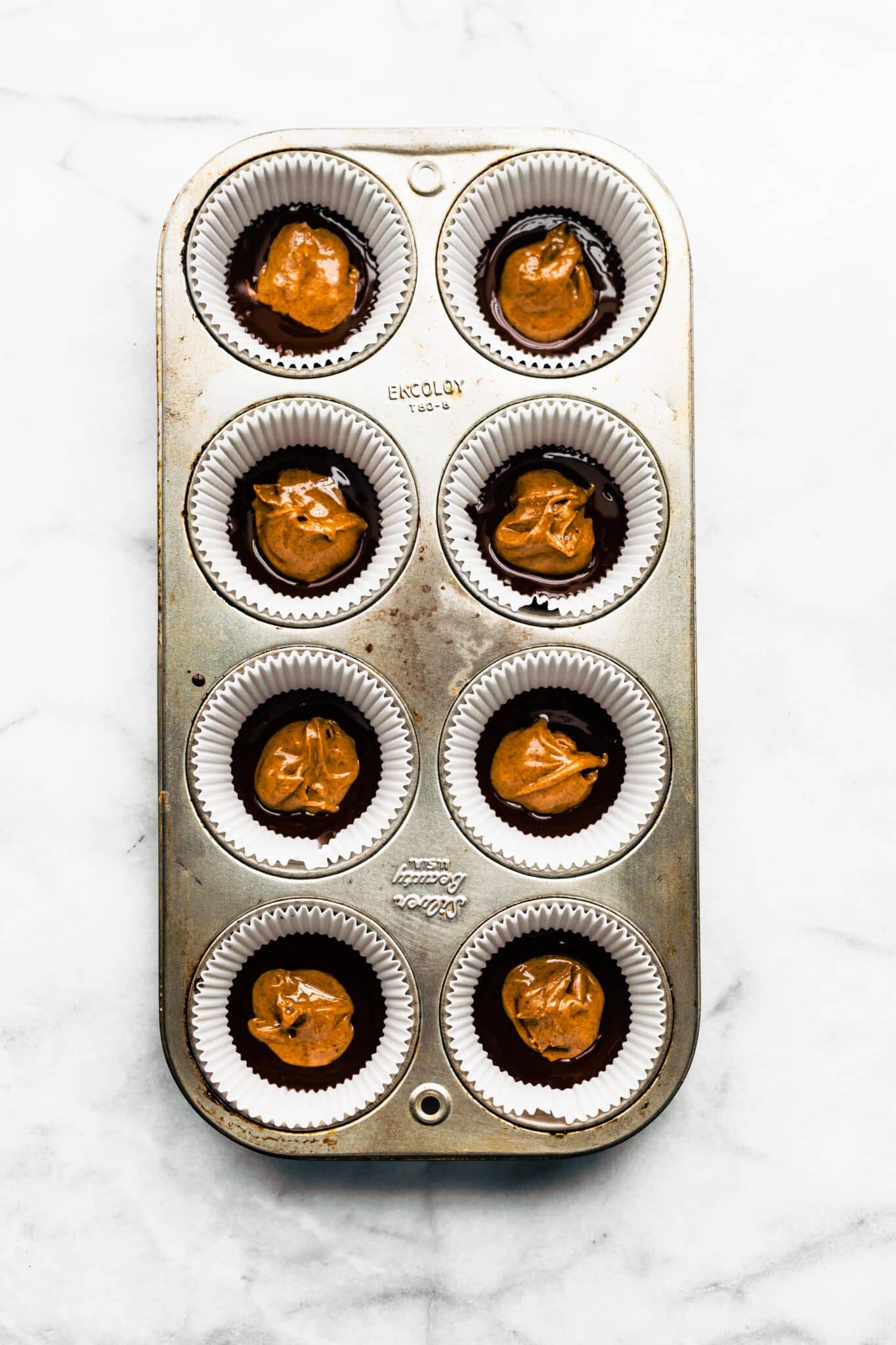 Eight muffin cup liners in a pan with almond butter on top of melted chocolate.