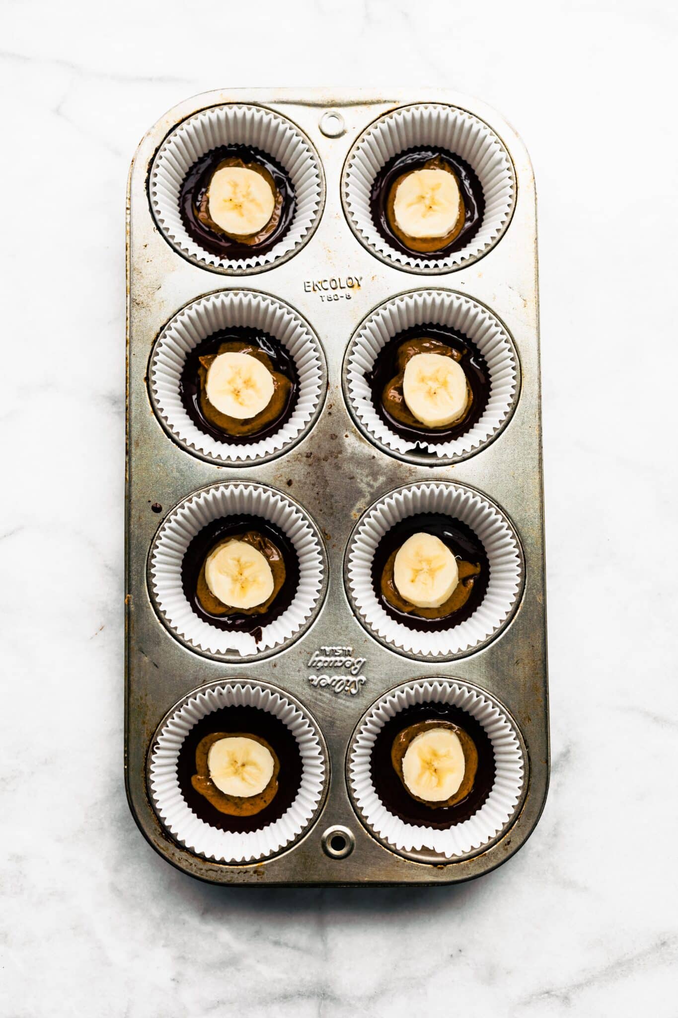 Eight muffin cups filled with dark chocolate, almond butter and a banana slice.