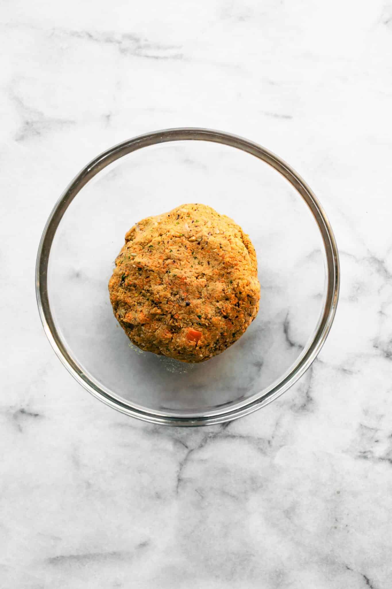 Vegan veggie burger batter shaped into a ball in a glass mixing bowl.