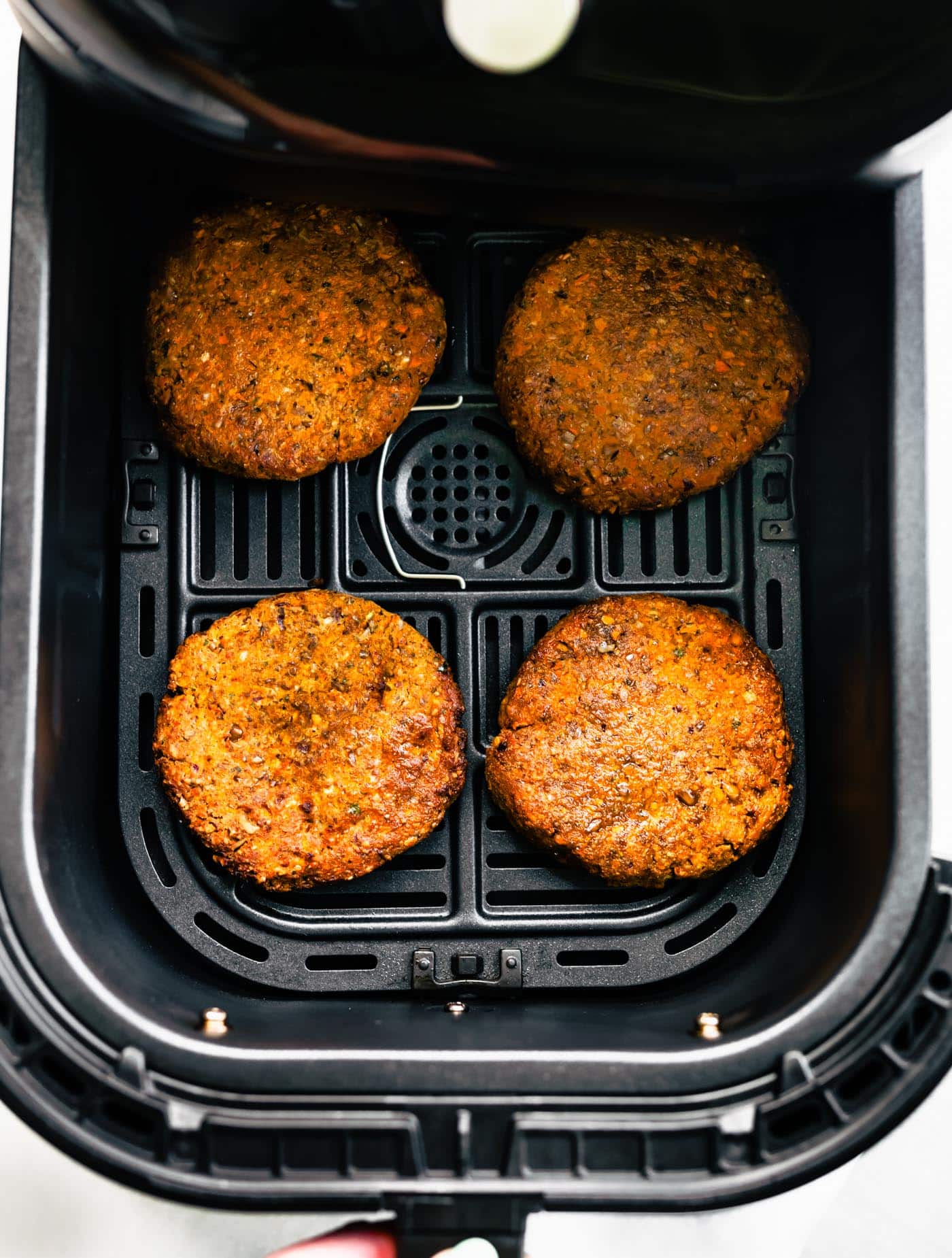 Four golden brown baked veggie burgers in an air fryer basket.