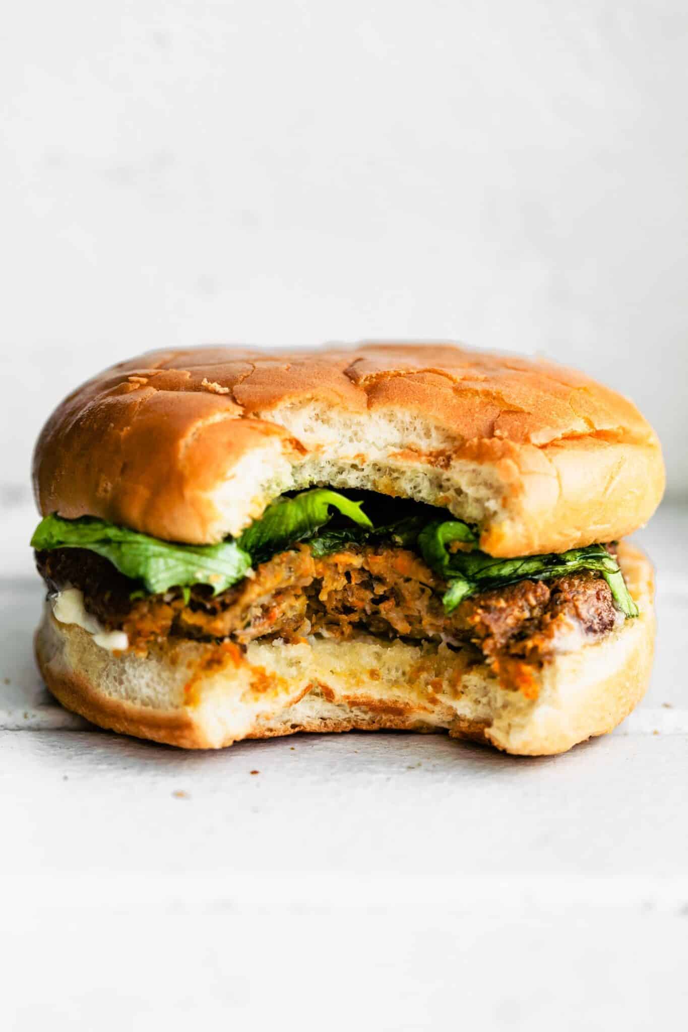 A bite taken out of a vegan burger and lettuce in a gluten free hamburger bun.