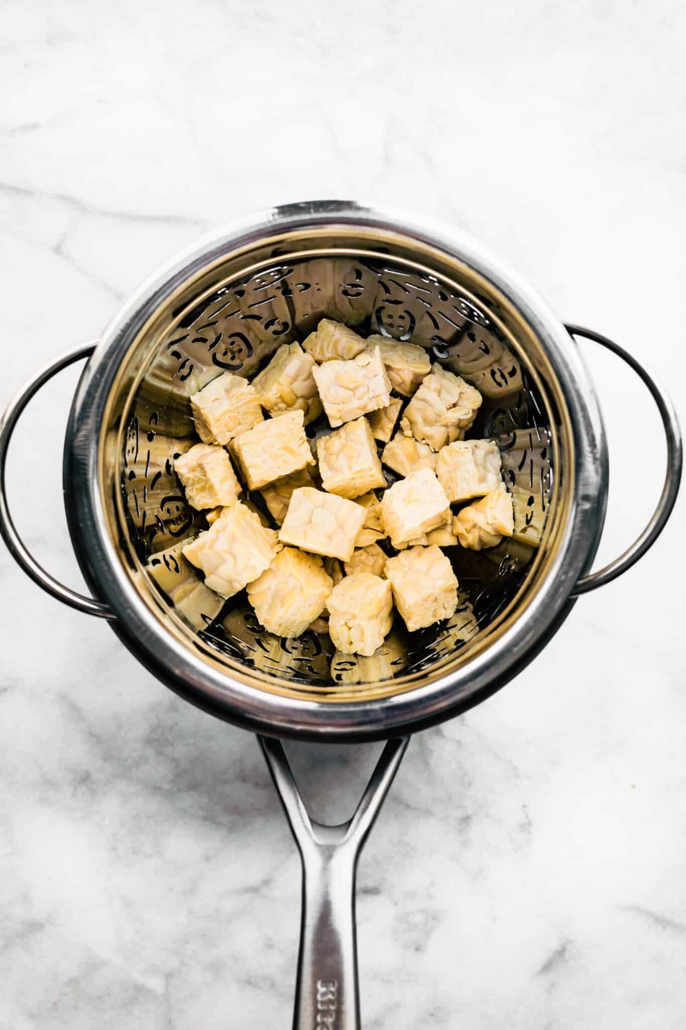 Cubed tempeh in a colander in a soup pot.