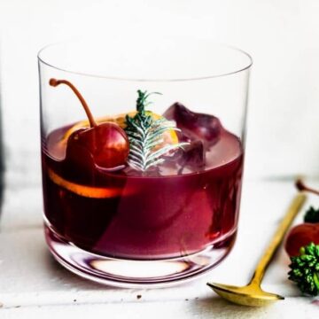 A short glass half filled with Yuletide Red Wine Cocktail garnished with orange slice and cherry.