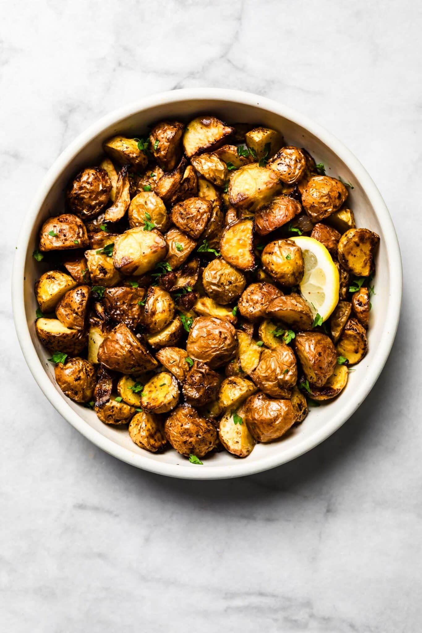 Air-fried baby potatoes in a white bowl garnished with parsley and a lemon slice.