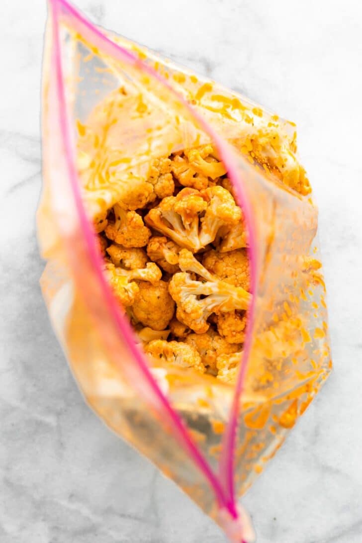Cauliflower florets coated in buffalo sauce in a gallon ziploc bag.