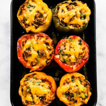 Overhead photo of six vegetarian stuffed bell peppers topped in a black casserole dish.