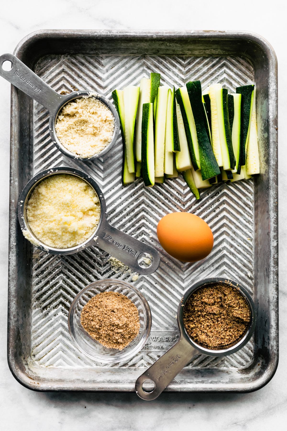 Ingredients to make gluten-free air fryer zucchini fries on a baking sheet.