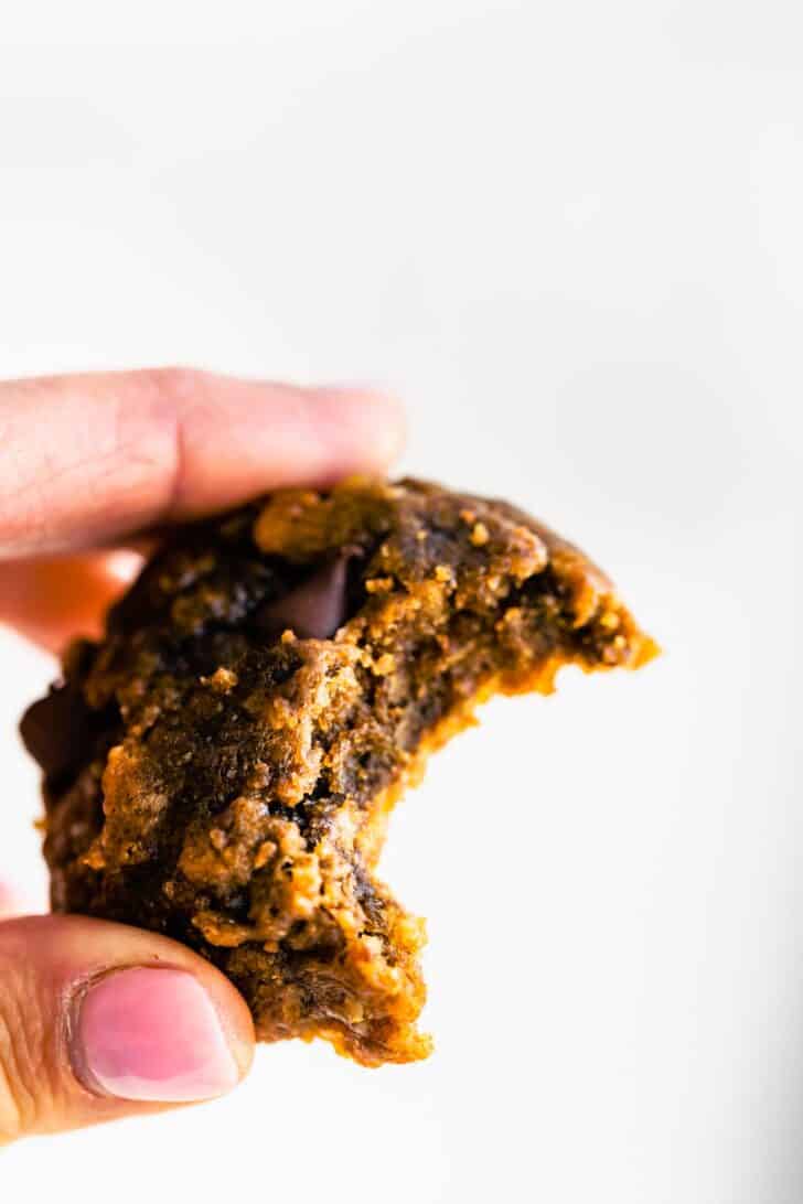 A woman's fingers holding up a banana breakfast cookie with a bite taken out.