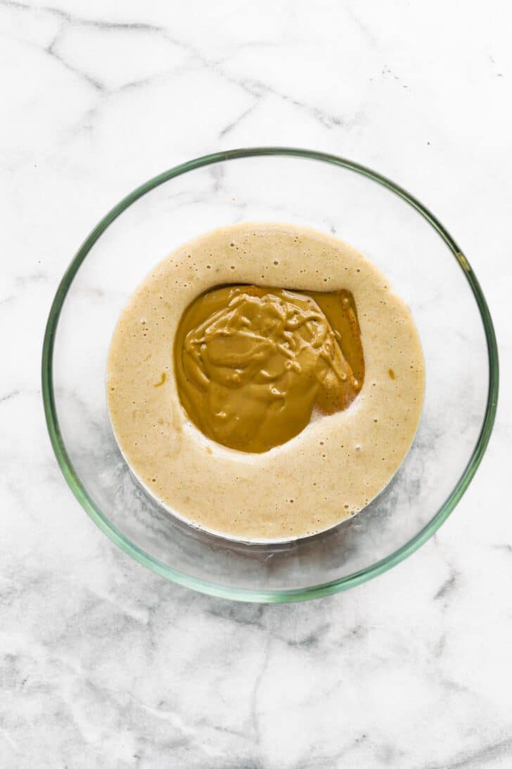 Almond butter sitting atop a mixture of banana and eggs in a glass bowl.