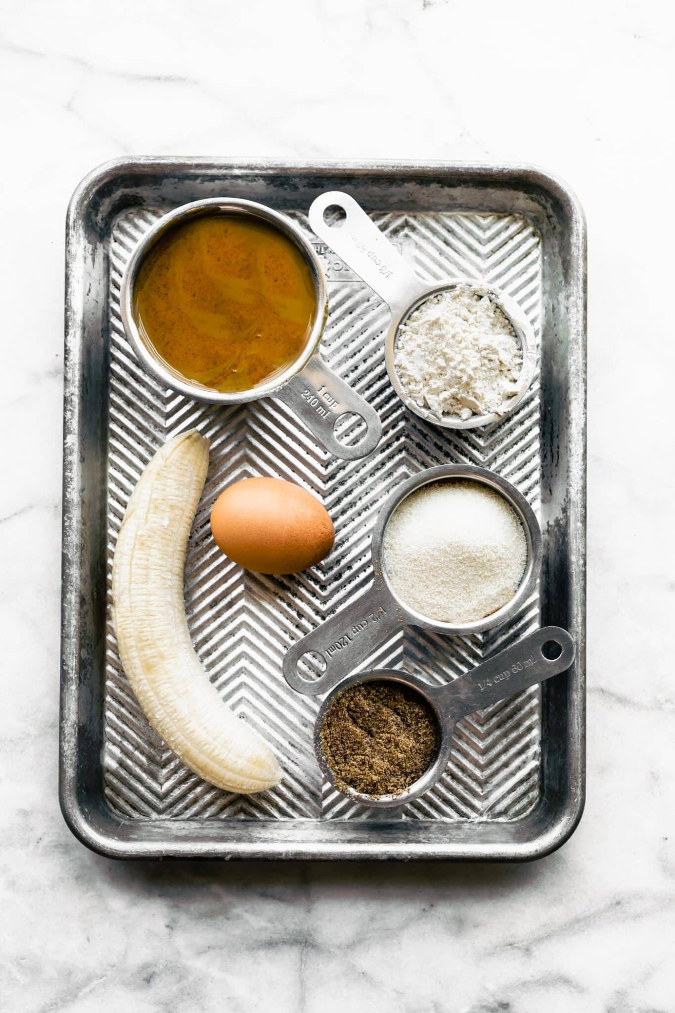 Overhead photo of a sheet pan with cups of ingredients for banana cookies.
