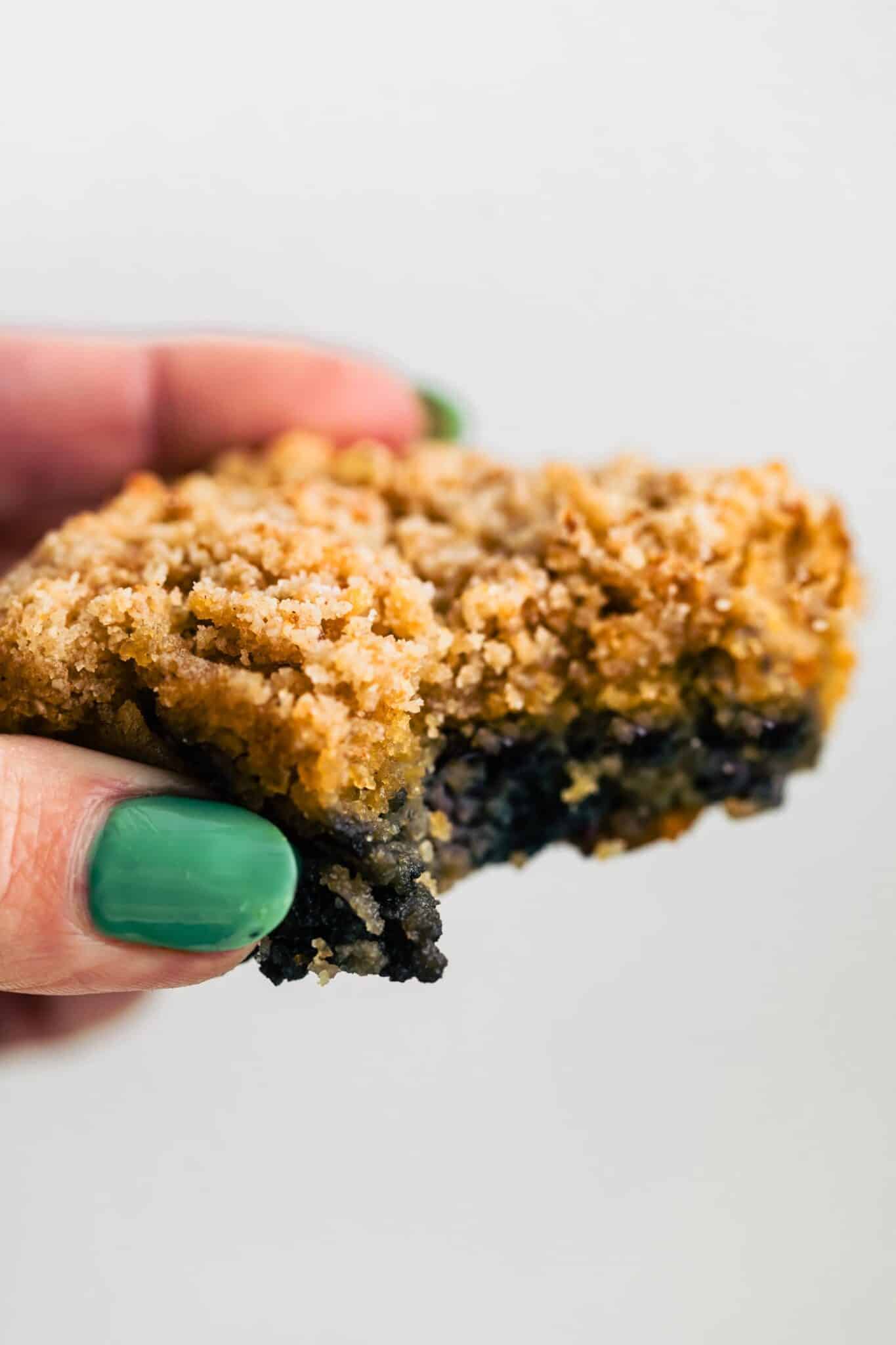 woman's hands holding an almond flour blueberry cake with a bite out of it