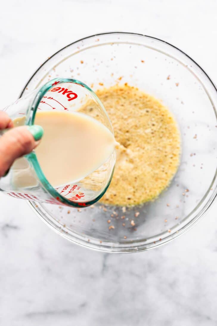 woman's hands pouring milk into a bowl of whisked eggs