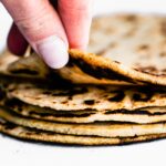 A hand grabbing an almond flour tortilla from a stack of tortillas.
