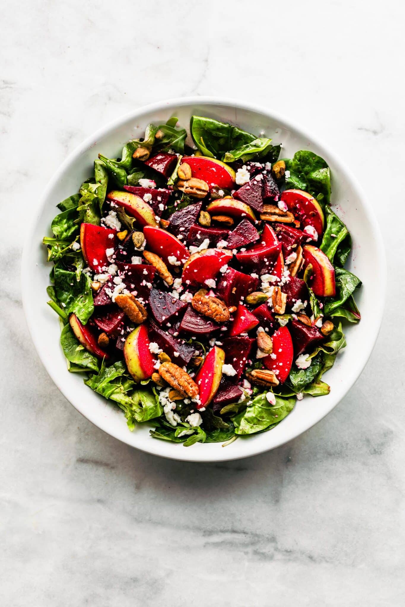 chopped apple and marinated beet salad in a white bowl with nuts on top