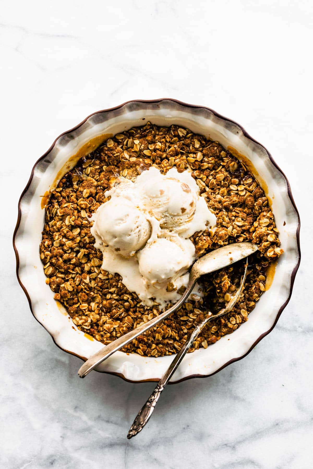 Baked gluten free apple crisp topped with vanilla ice cream and two serving spoons.