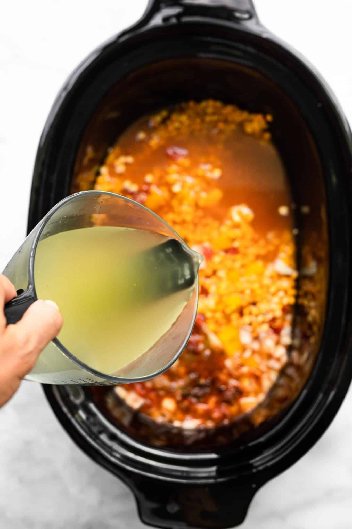 Vegetable broth being poured into a crock pot.
