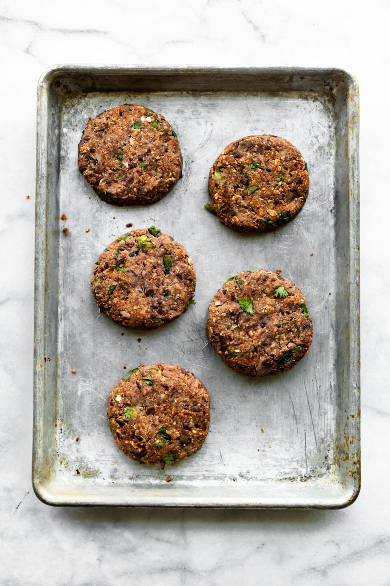 Five raw black bean burgers on a metal baking sheet.