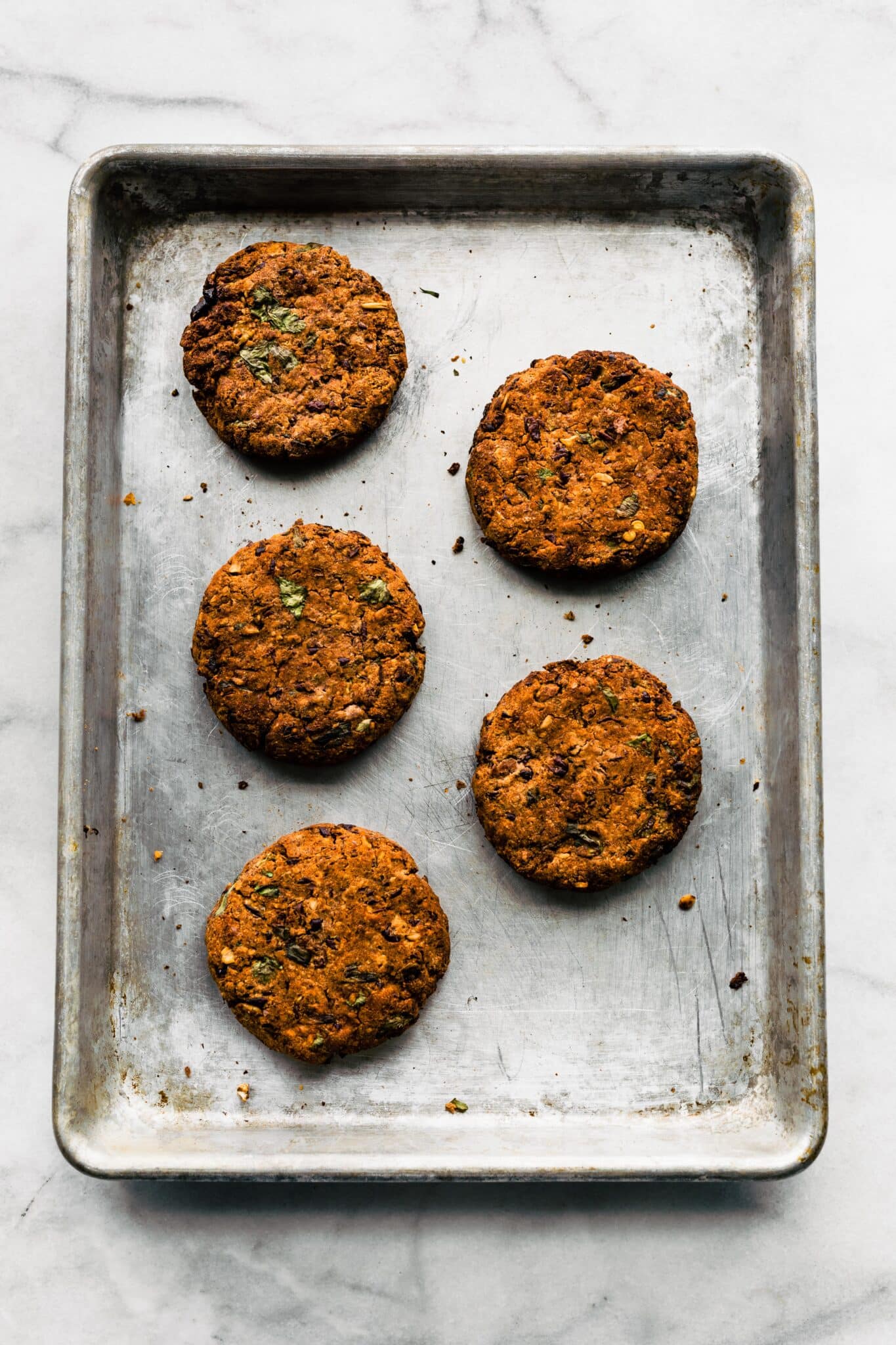 Five grilled black bean burgers on a metal baking sheet.