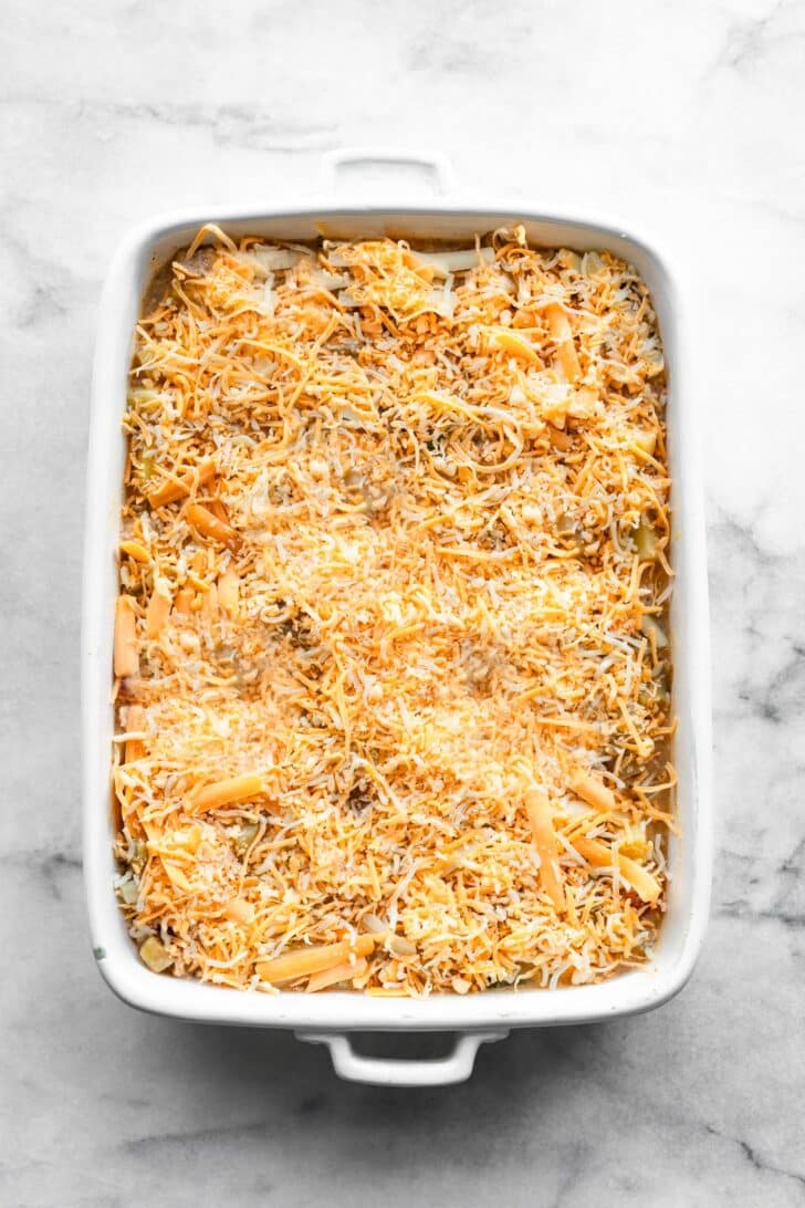 Rectangular baking dish filled with the uncooked breakfast casserole mixture, evenly topped with a layer of shredded cheese.