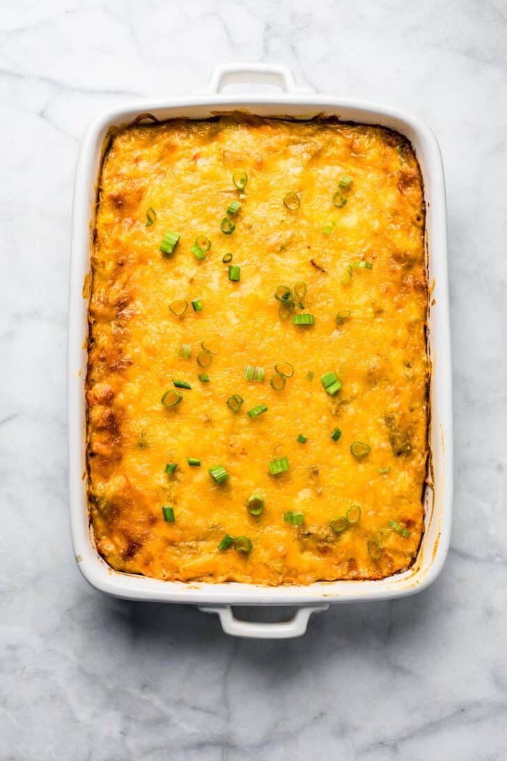 baked cheesy breakfast casserole in a white baking dish with chopped green onion on top