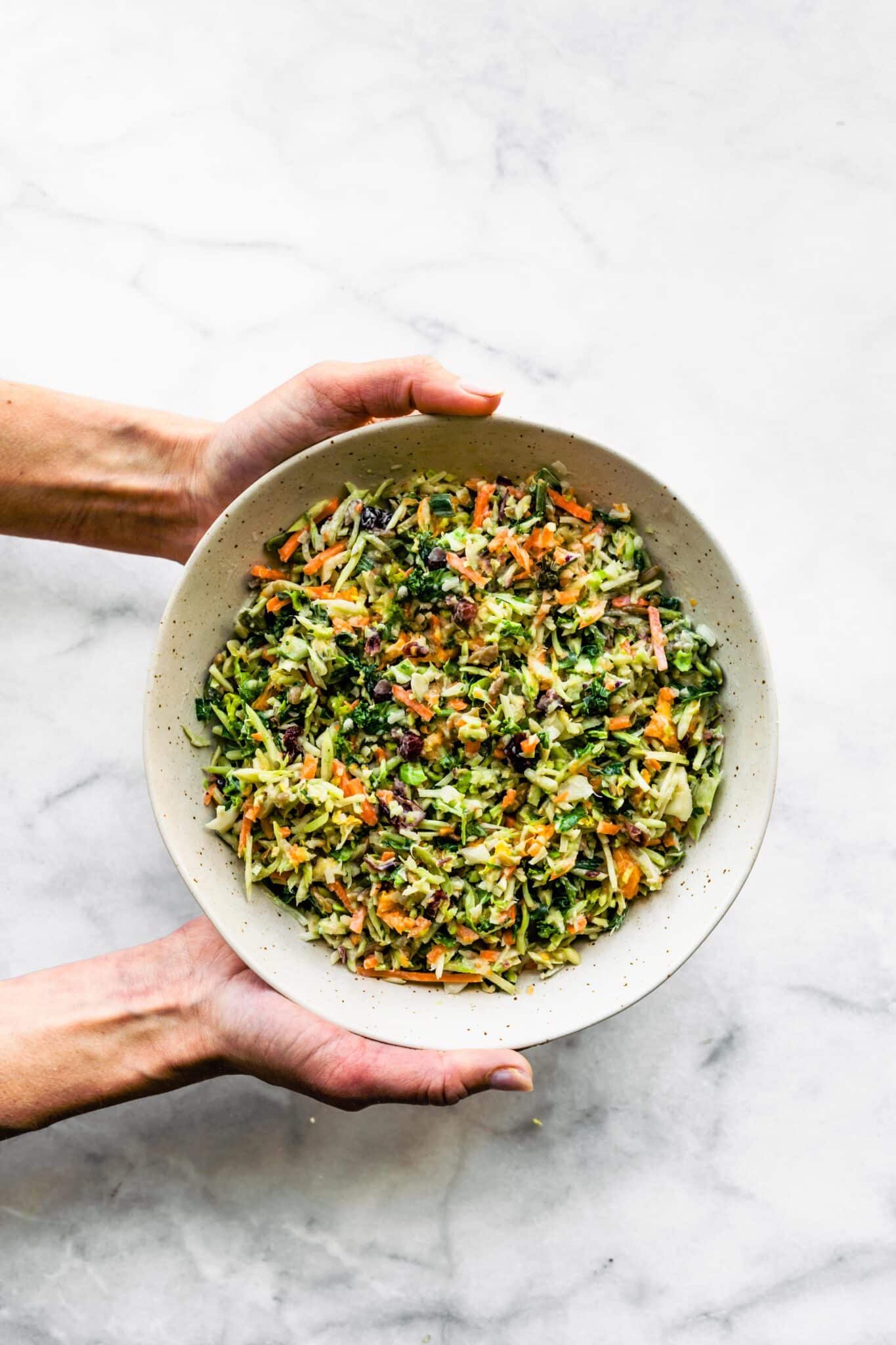 A woman's hands holding a bowl filled with a broccoli slaw salad.