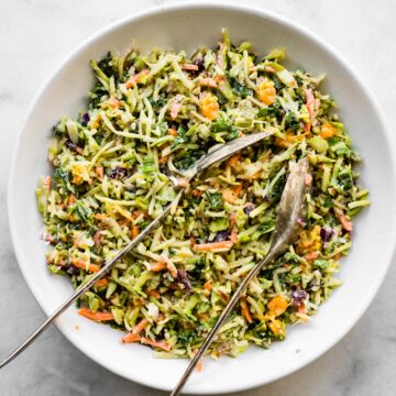 Overhead photo of a healthy broccoli slaw in a white bowl with two spoons.