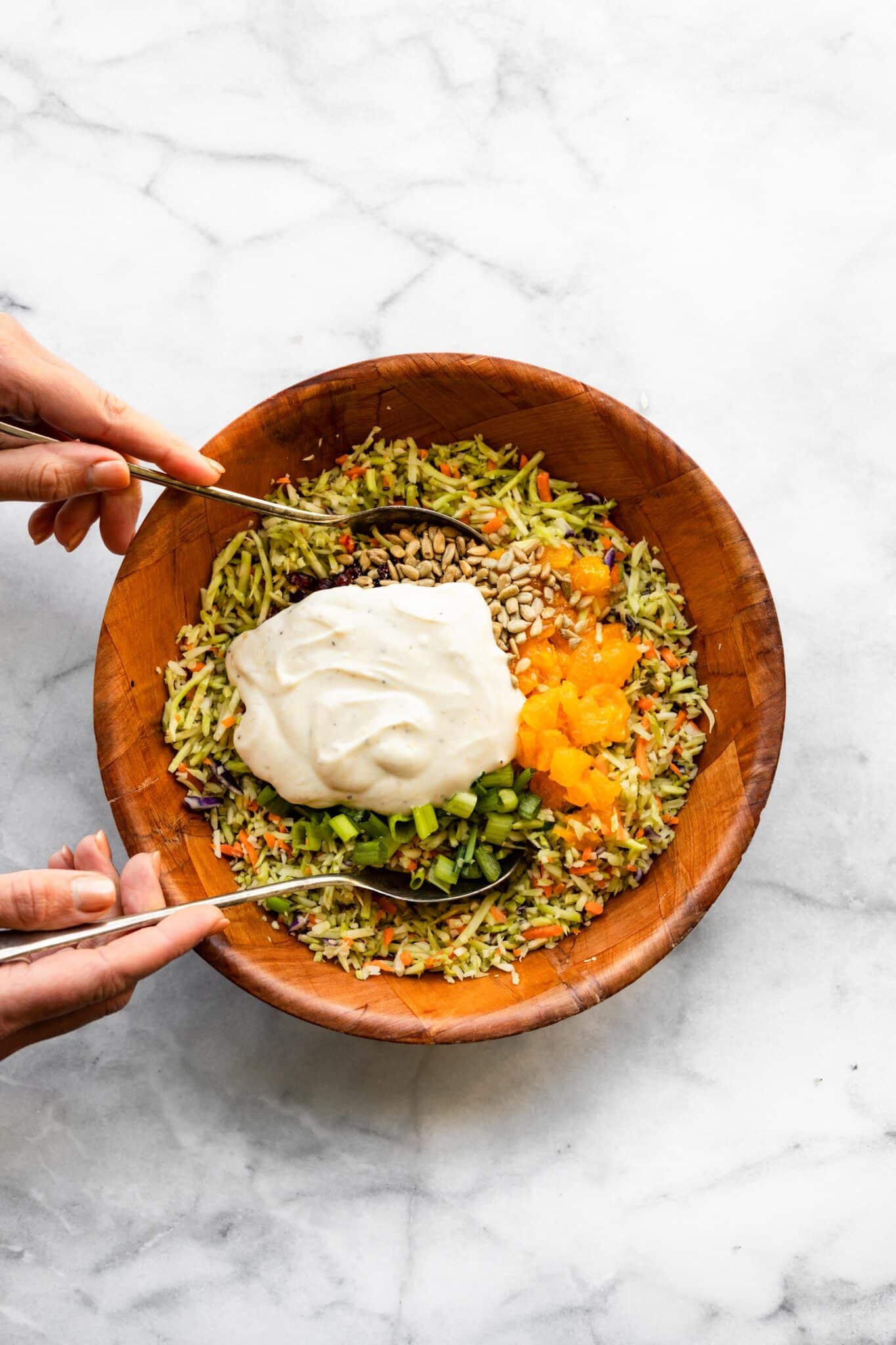 Two spoons starting to mix a yogurt sauce into broccoli slaw.