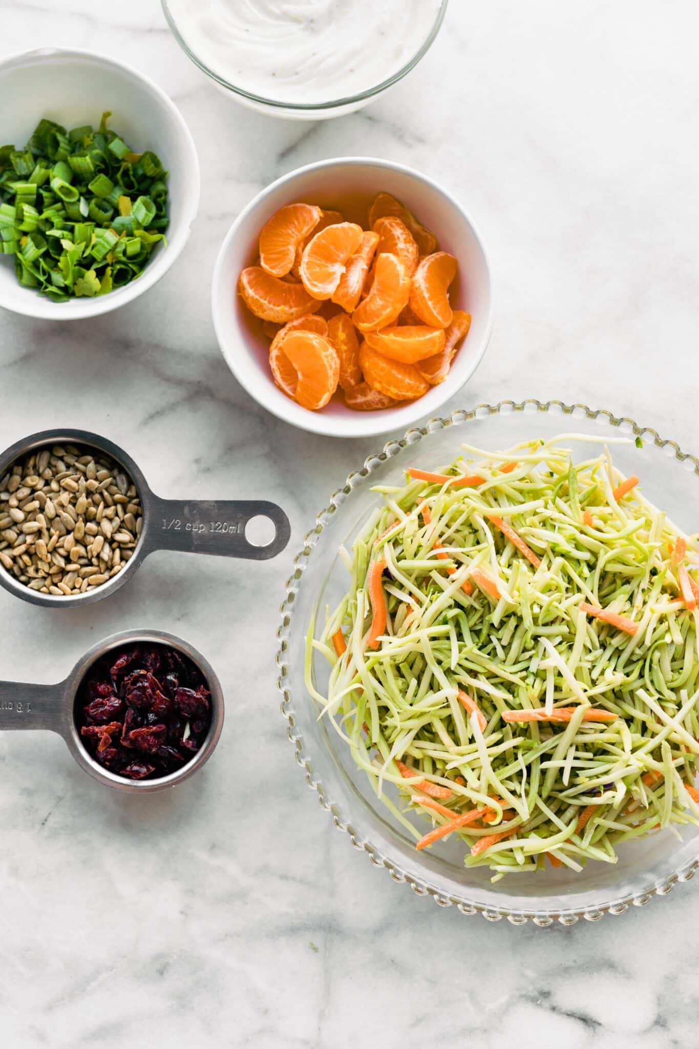 Overhead photo of ingredients for broccoli slaw in separate bowls on a countertop.