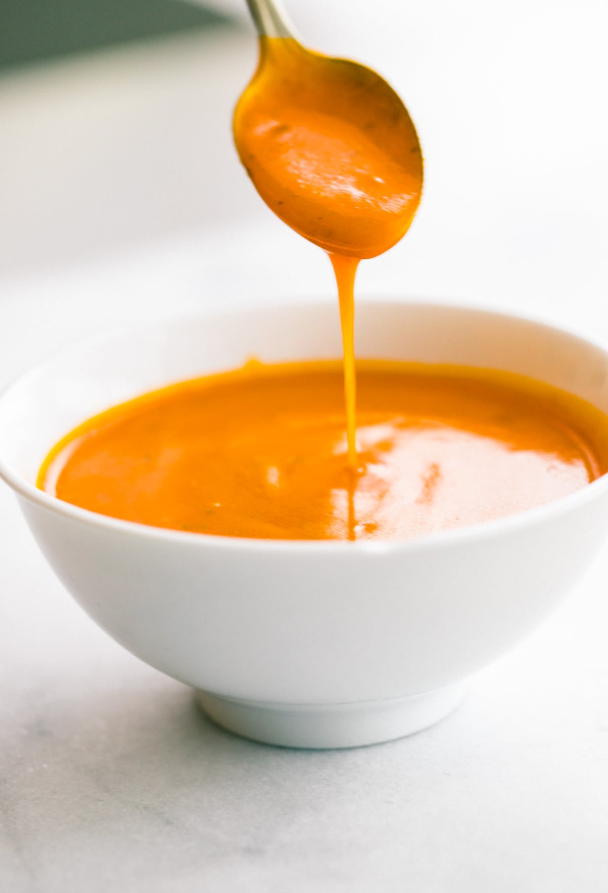 spicy buffalo sauce dripping off spoon into white bowl