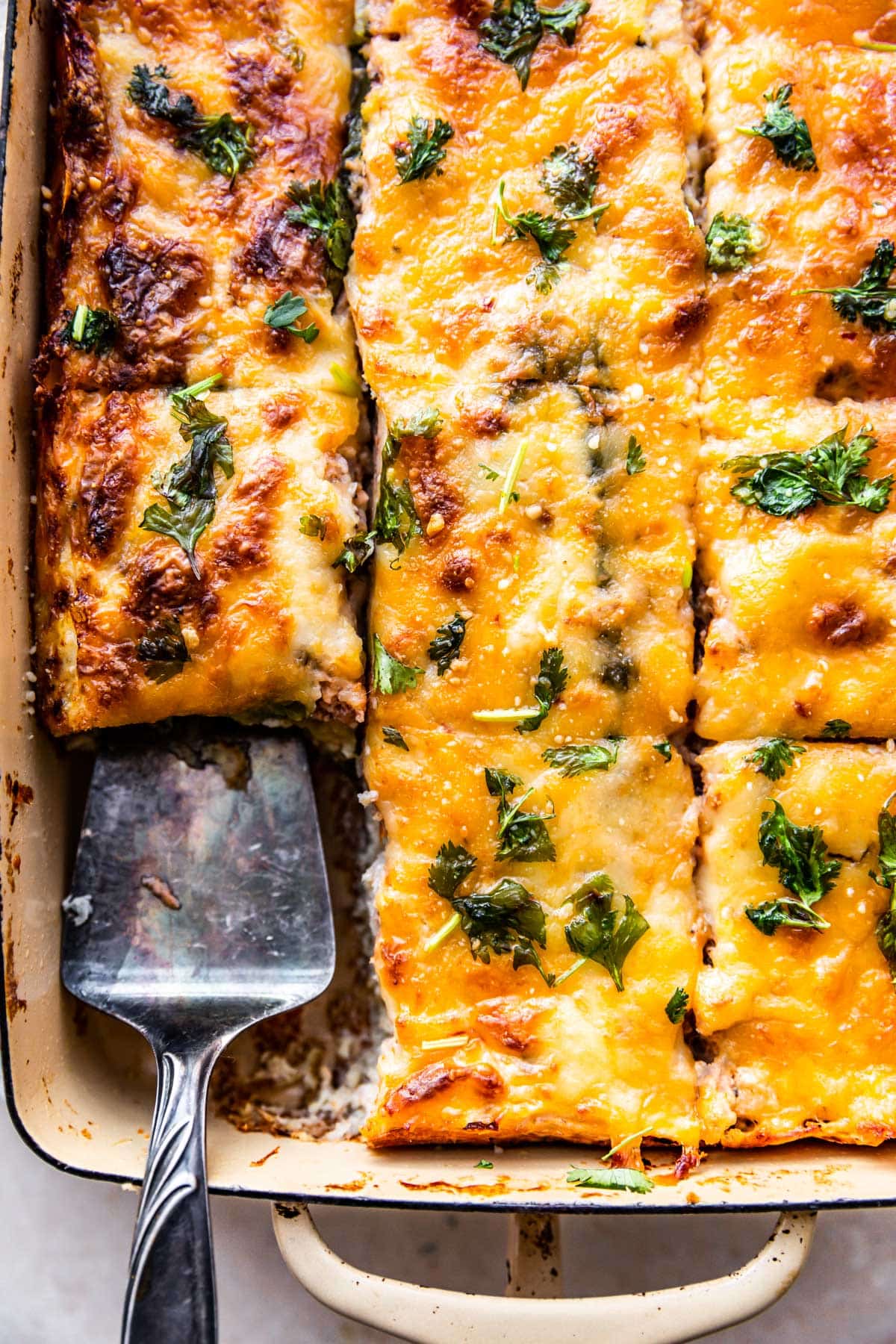 a serving utensil in a casserole dish with tex-mex egg and cauliflower casserole lifitng a piece out