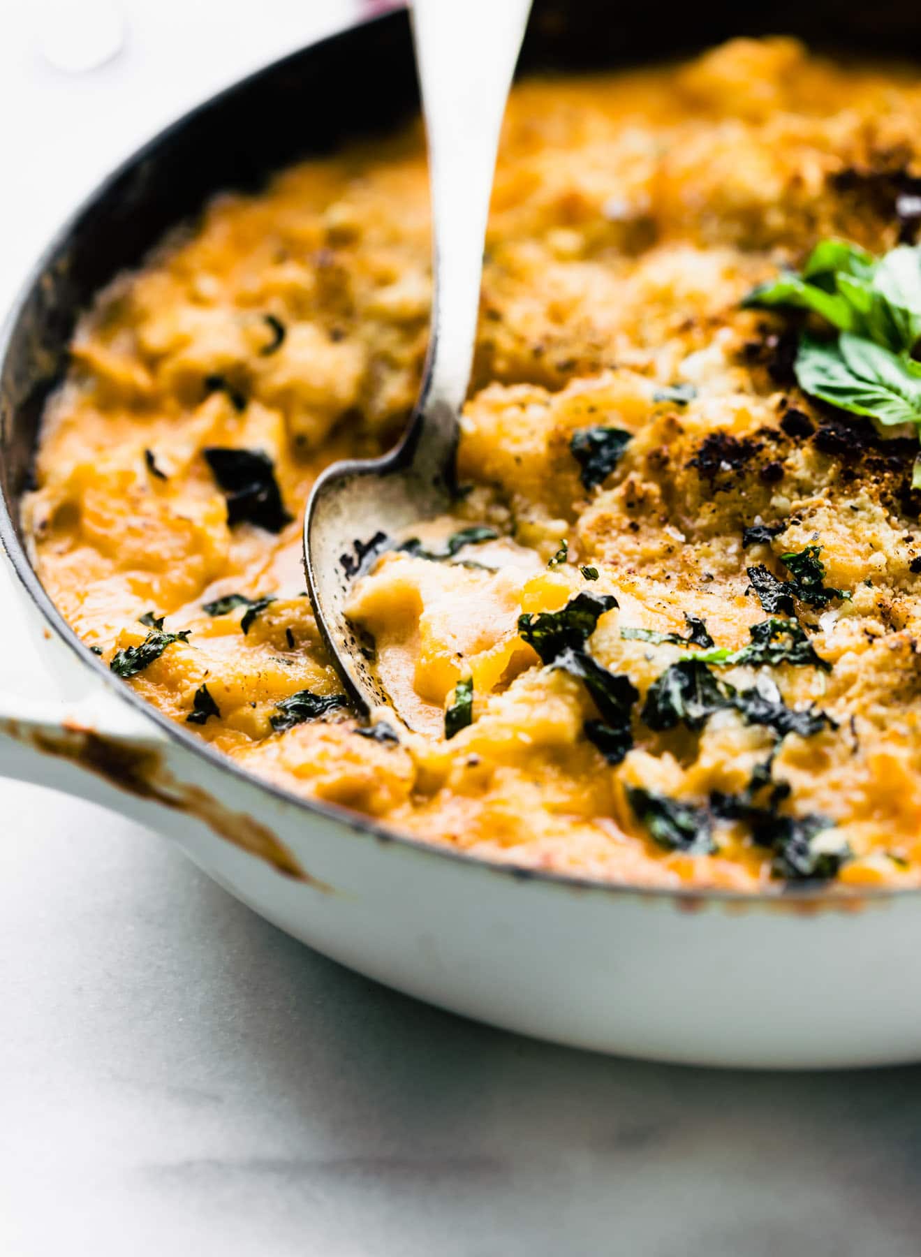 close up side view: serving spoon in white skillet of cheesy cauliflower baked casserole