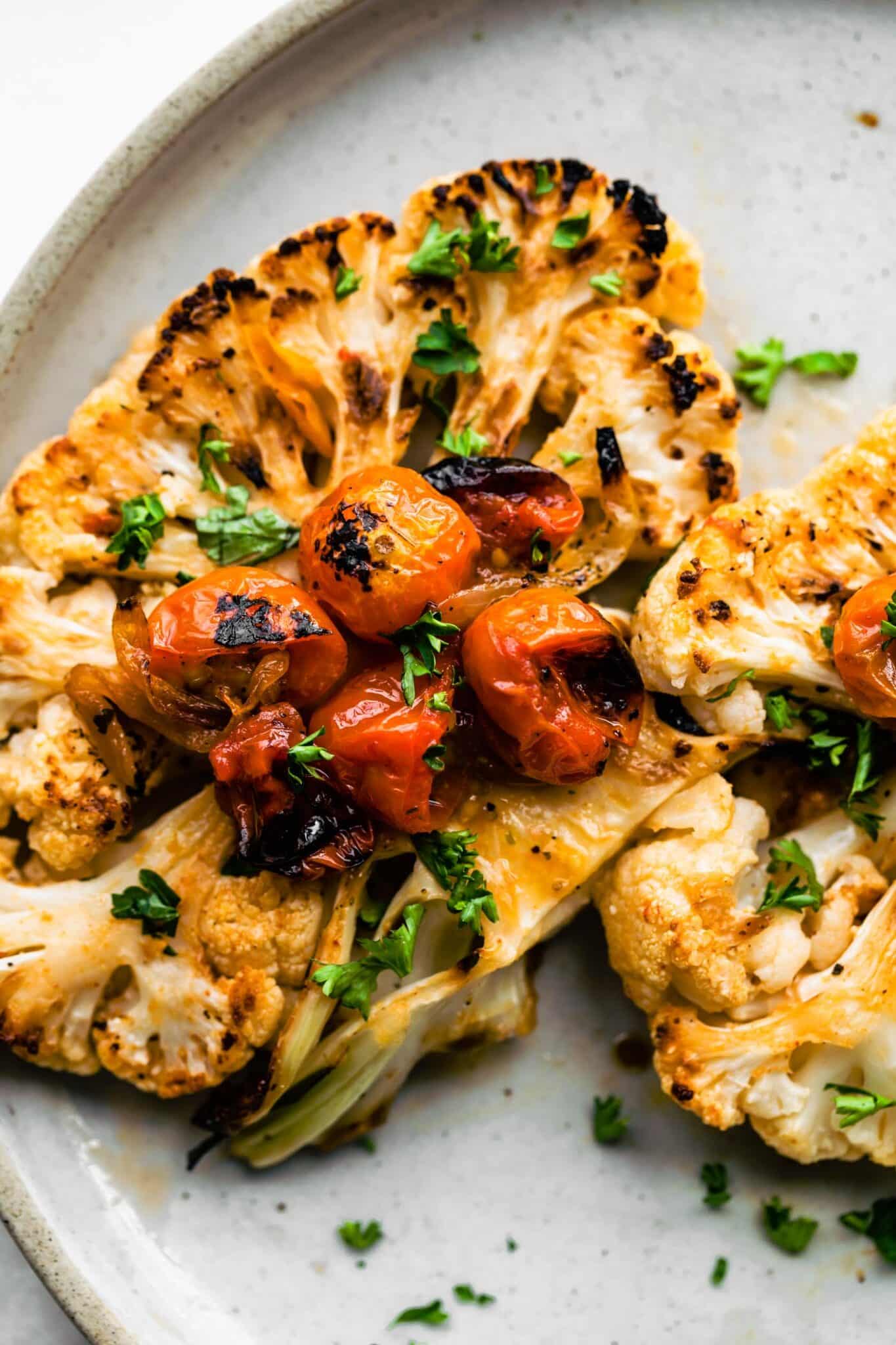 Roasted cauliflower steak on a light blue plate with blistered tomatoes and chopped herbs.