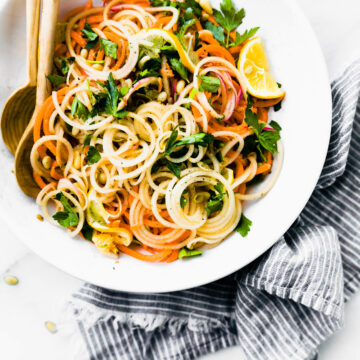 Overhead view carrot and celery root spiralized 'noodles' salad in white bowl.