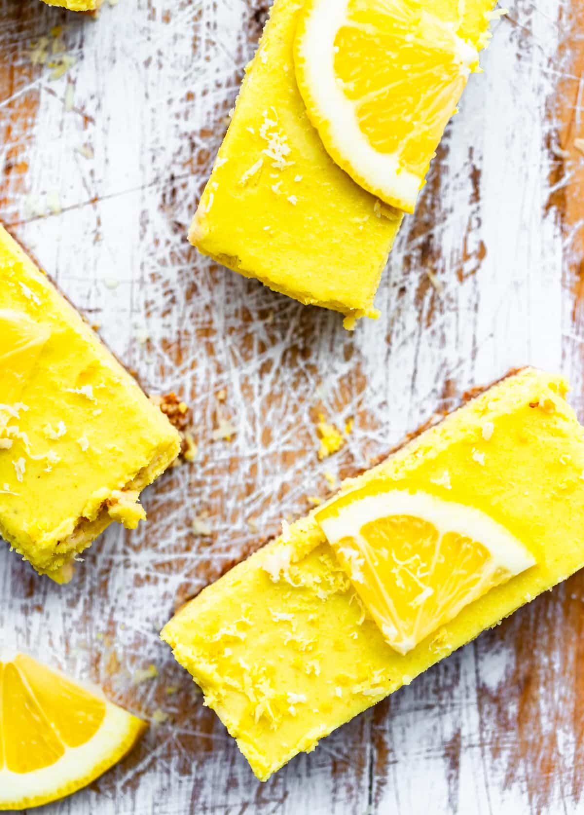 No Bake Lemon Cheesecake Bars topped with a lemon on white wood background