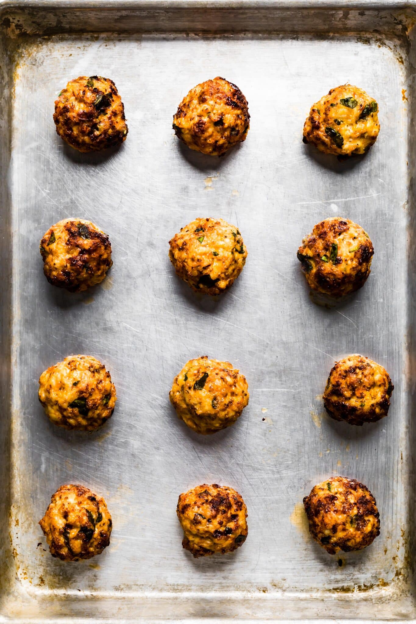 Overhead photo of twelve cooked gluten free chicken meatballs on a sheet pan.