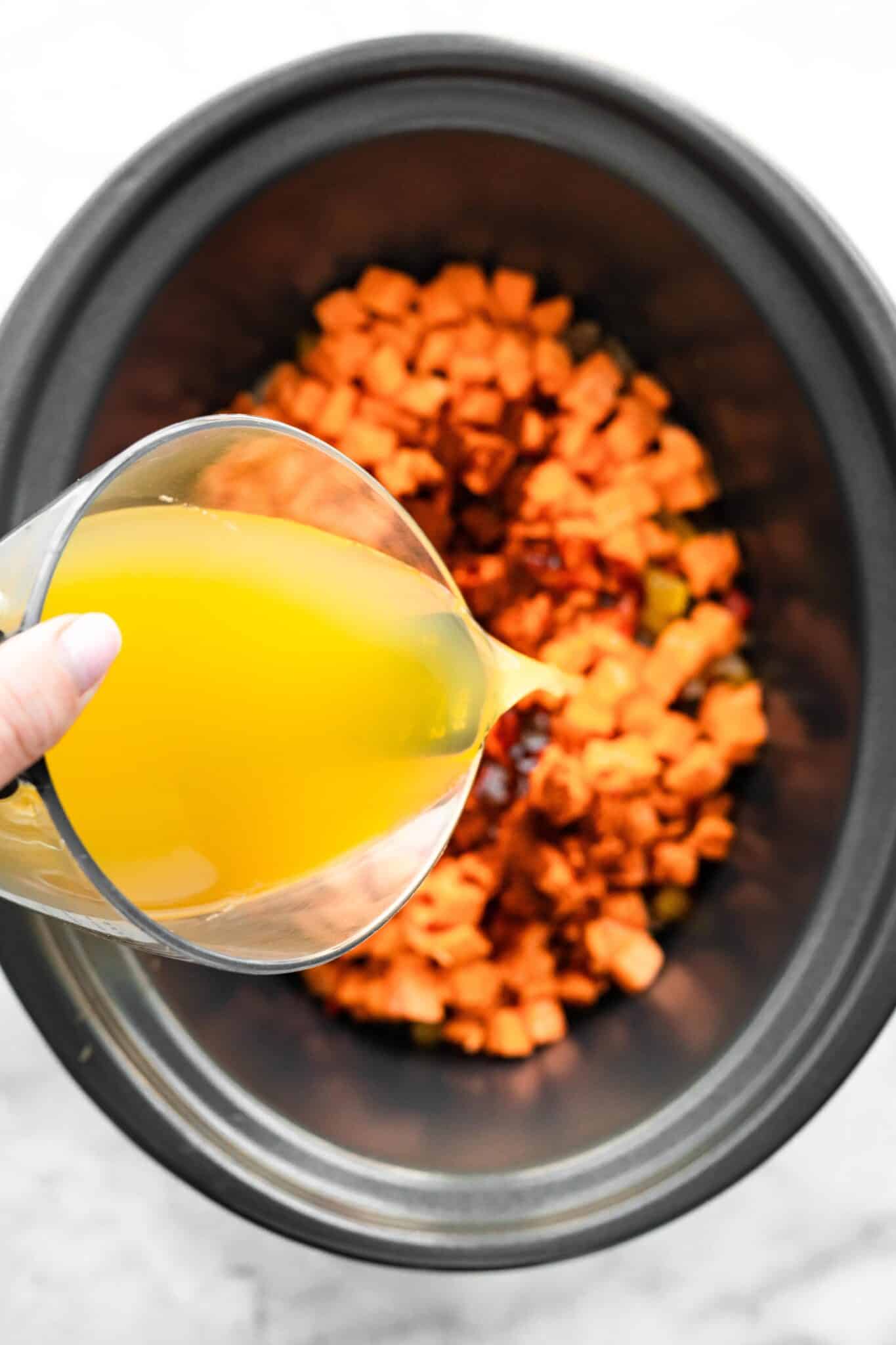 Overhead photo of chicken broth being poured into a crockpot of chili ingredients.