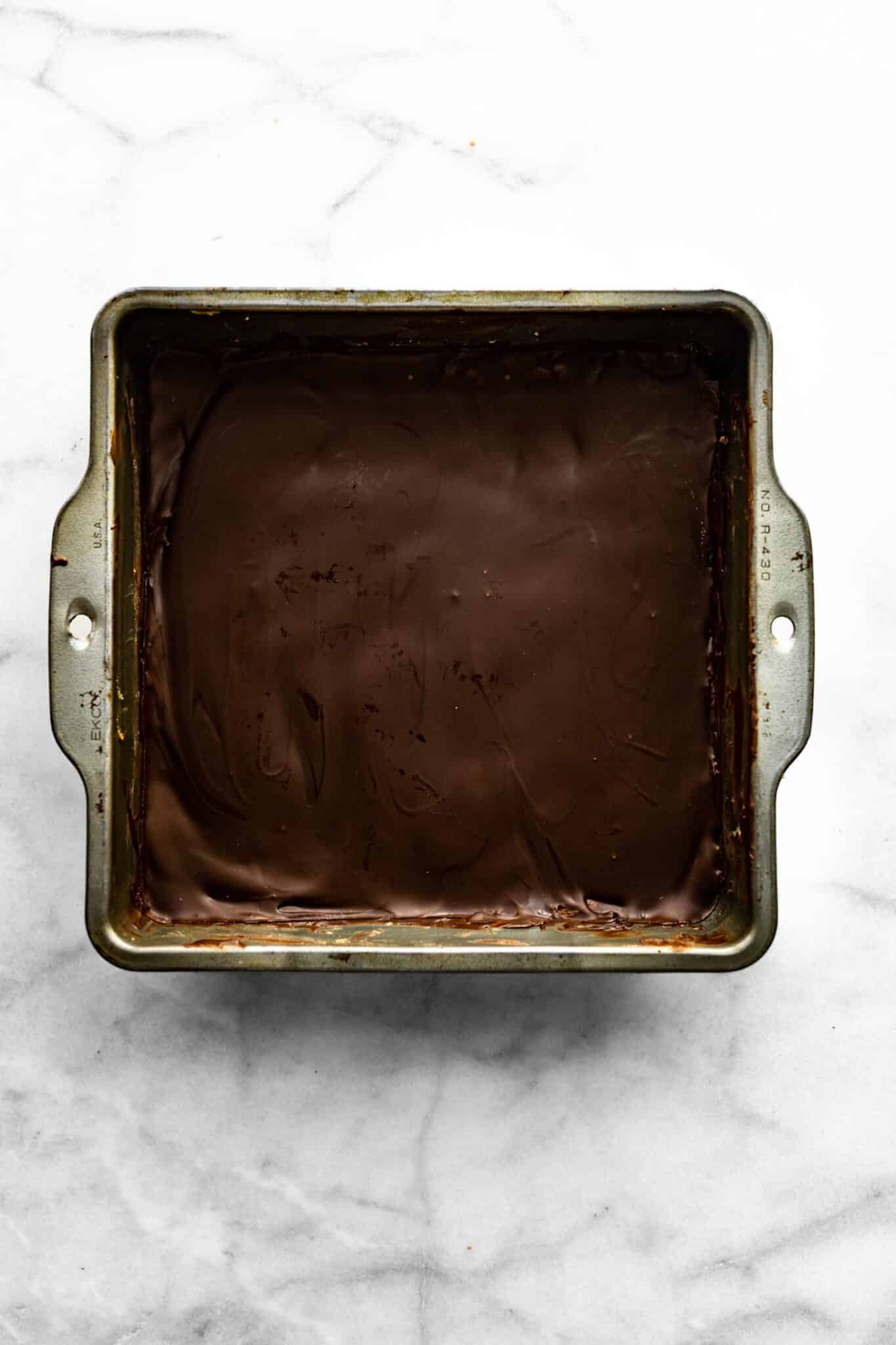 Melted chocolate covering an 8x8 pan of protein bars.