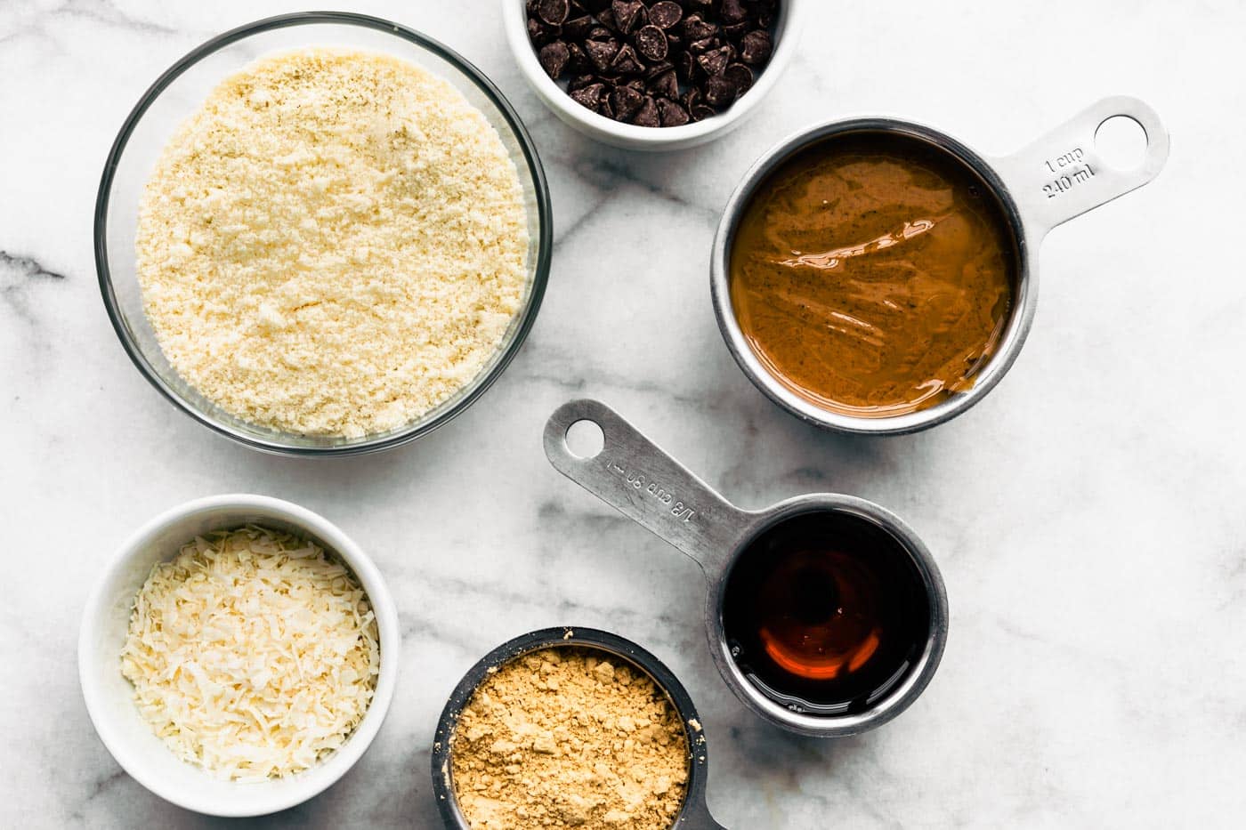 Ingredients in bowls and measuring cups for no bake chocolate almond flour protein bars.