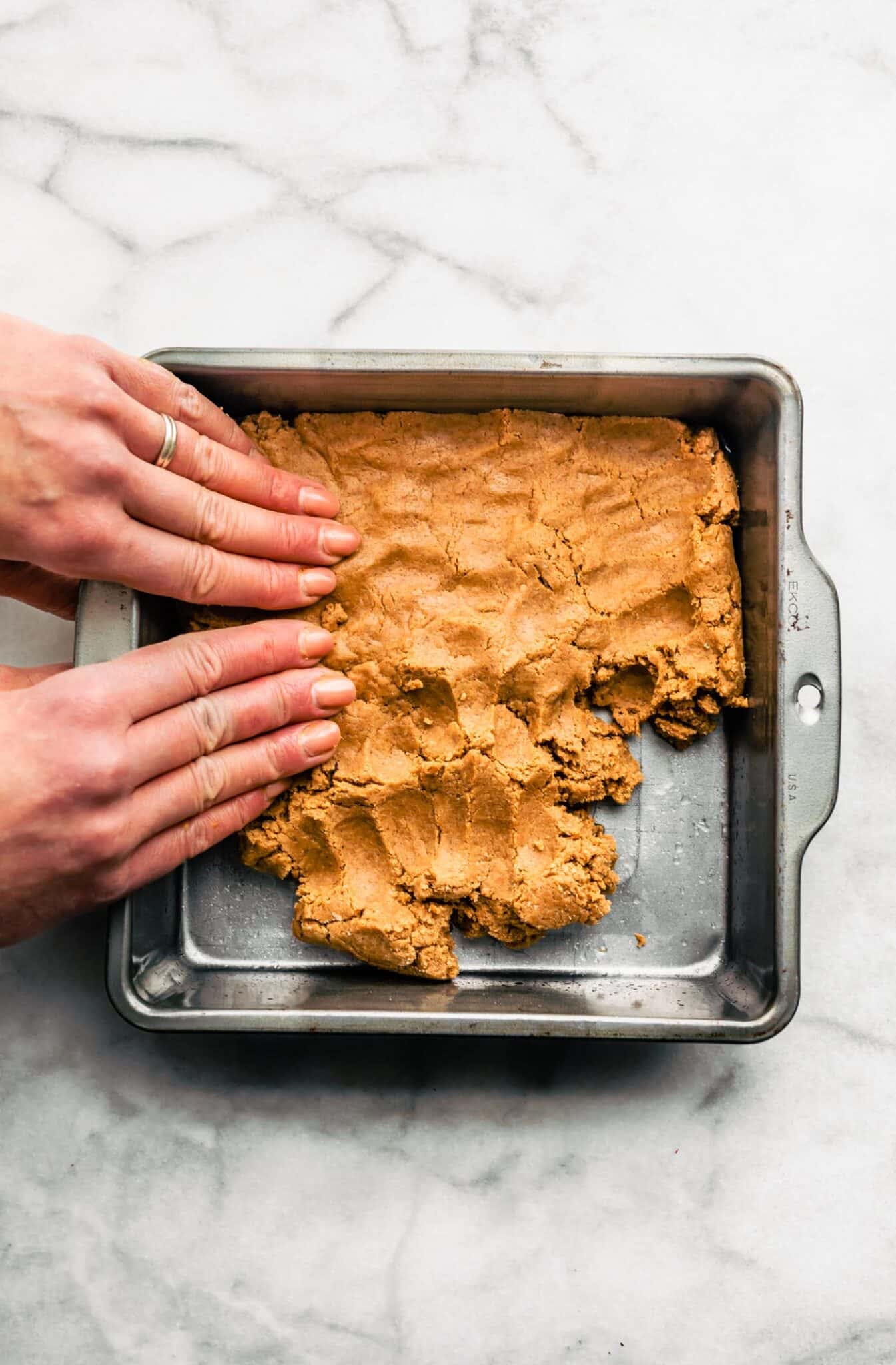 A woman's hands pressing almond flour dough into a metal pan.