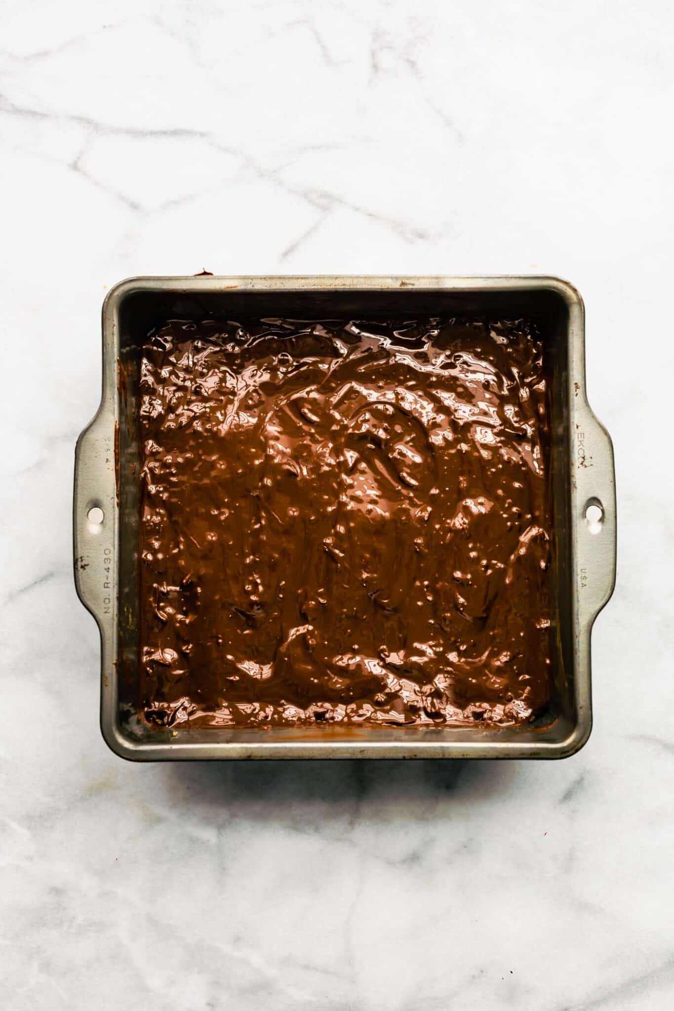 Melted chocolate spread over a pan of bars in a square metal pan.
