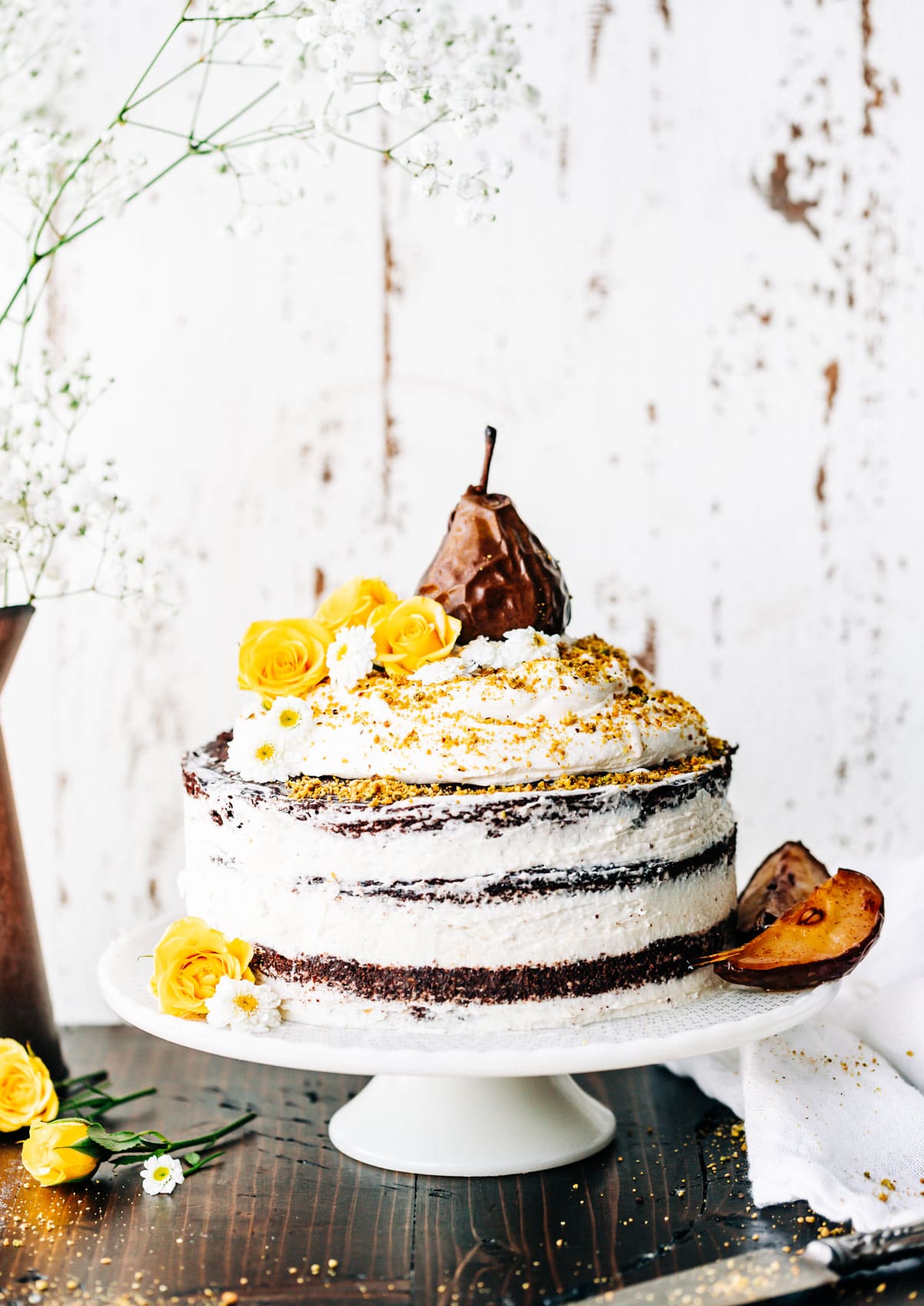 naked cake on platter with coconut frosting, edible flowers and a glazed pear on top