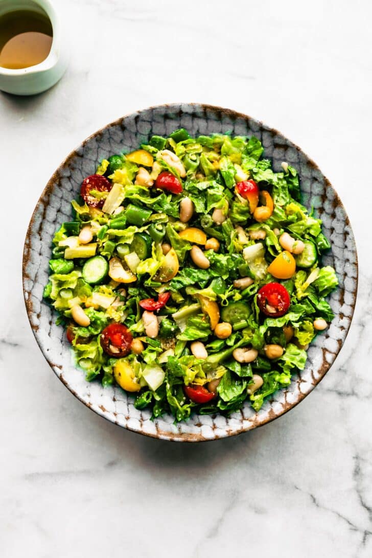 Blue bowl filled with chopped romaine salad, served with a small pourer of dressing on the side
