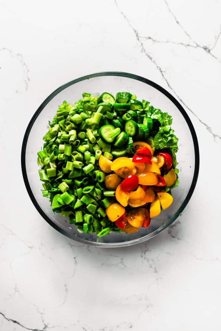 a bowl of chopped romaine lettuce topped with tomatoes and chopped snap peas .