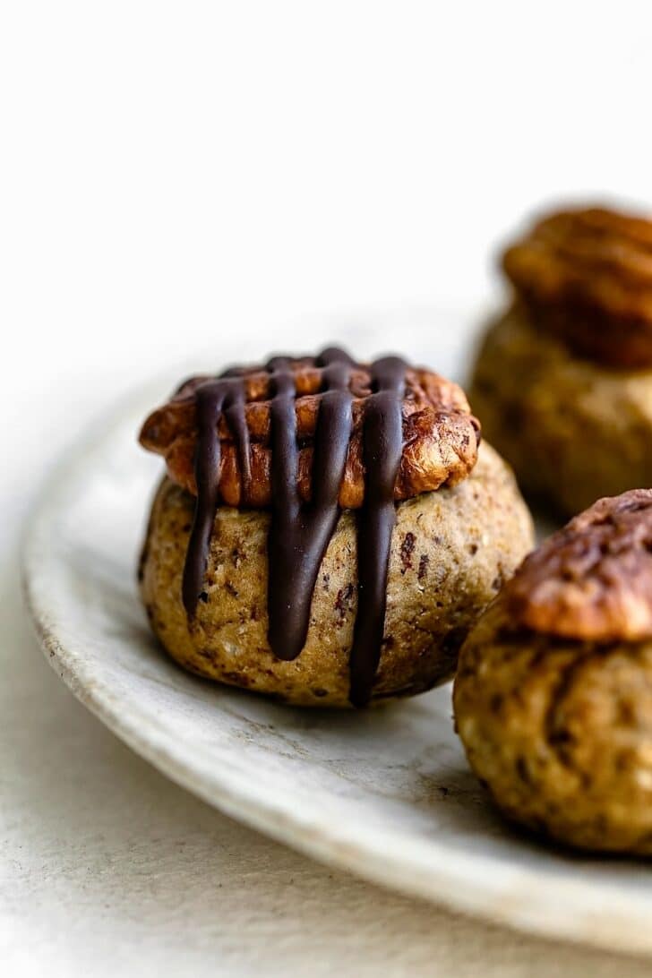 Close-up shot of pecan pie balls on a plate, highlighting the chocolate drizzle and pecan topping