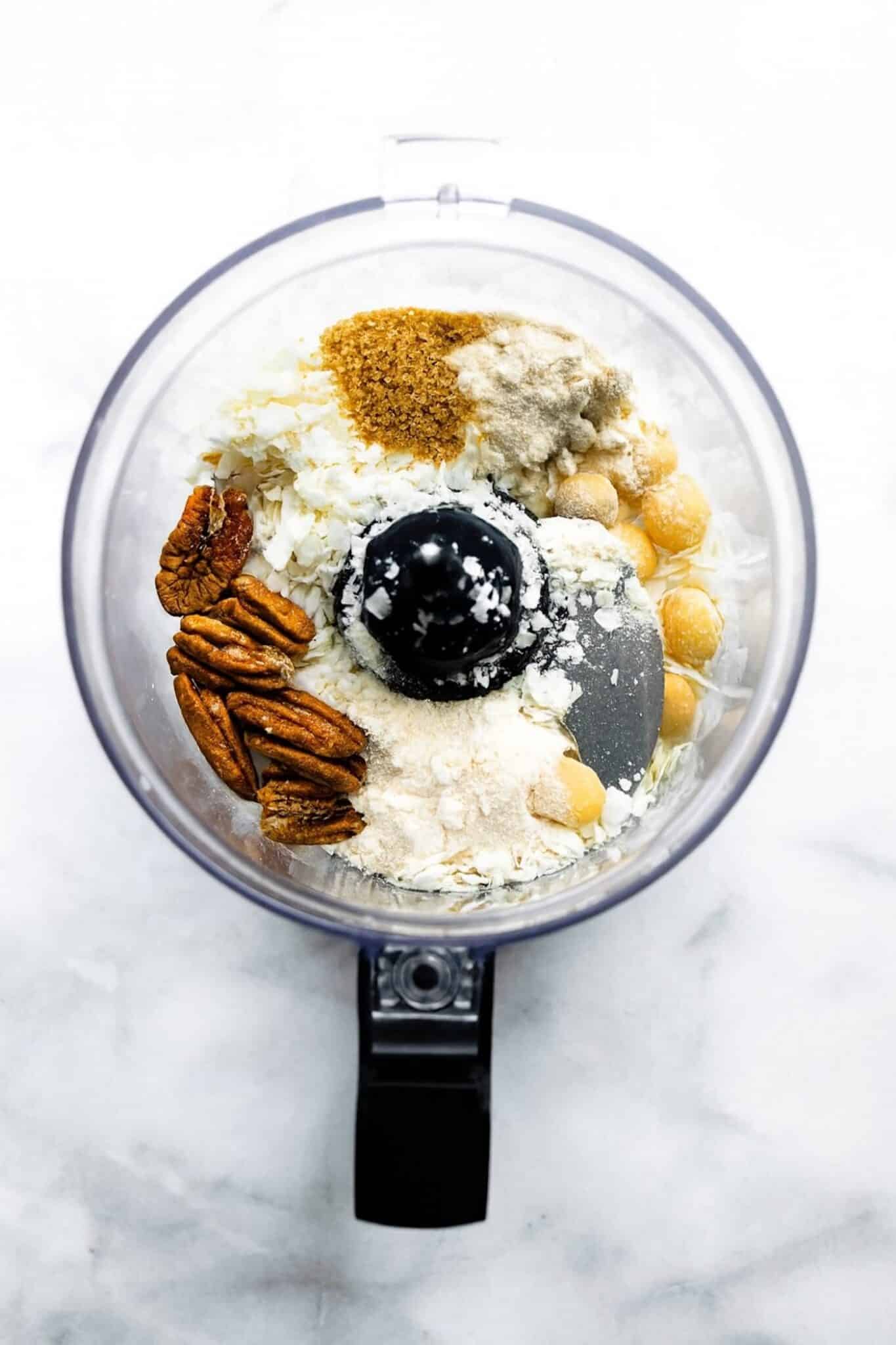 coconut, flour, pecans, macadamia nuts, and coconut sugar in the bowl of a food processor.